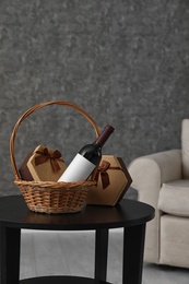 Photo of Wicker basket with bottle of wine and gift boxes on table in room. Space for design