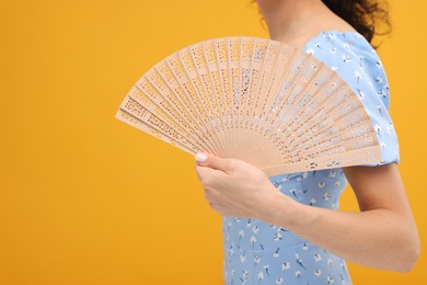Photo of Woman holding hand fan on orange background, closeup. Space for text