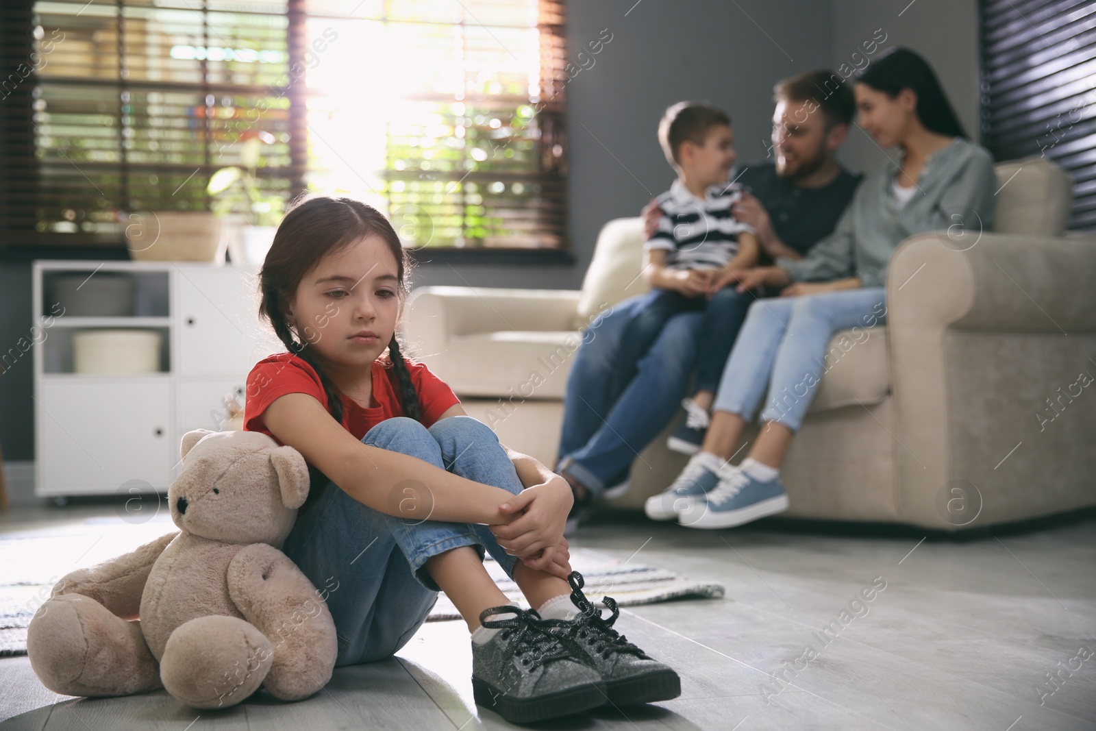 Photo of Unhappy little girl feeling jealous while parents spending time with her brother at home