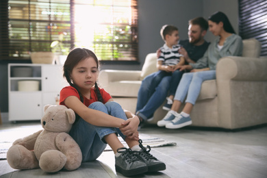 Photo of Unhappy little girl feeling jealous while parents spending time with her brother at home