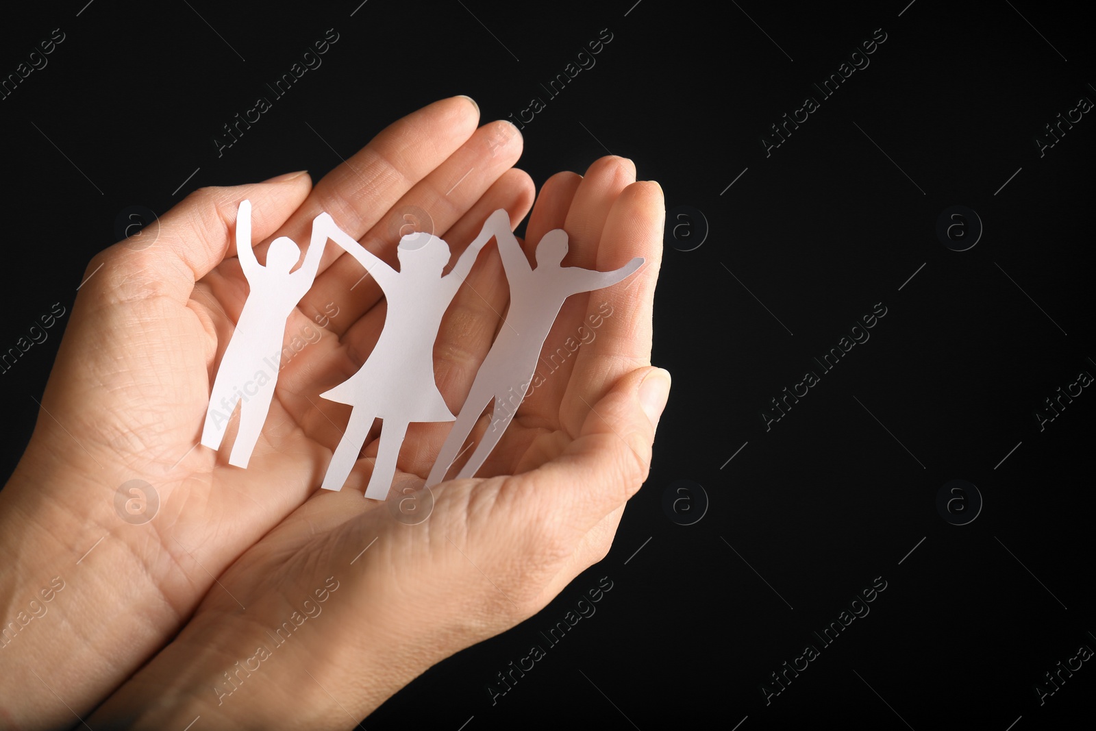 Photo of Woman holding paper silhouette of family in hands on black background, closeup. Space for text