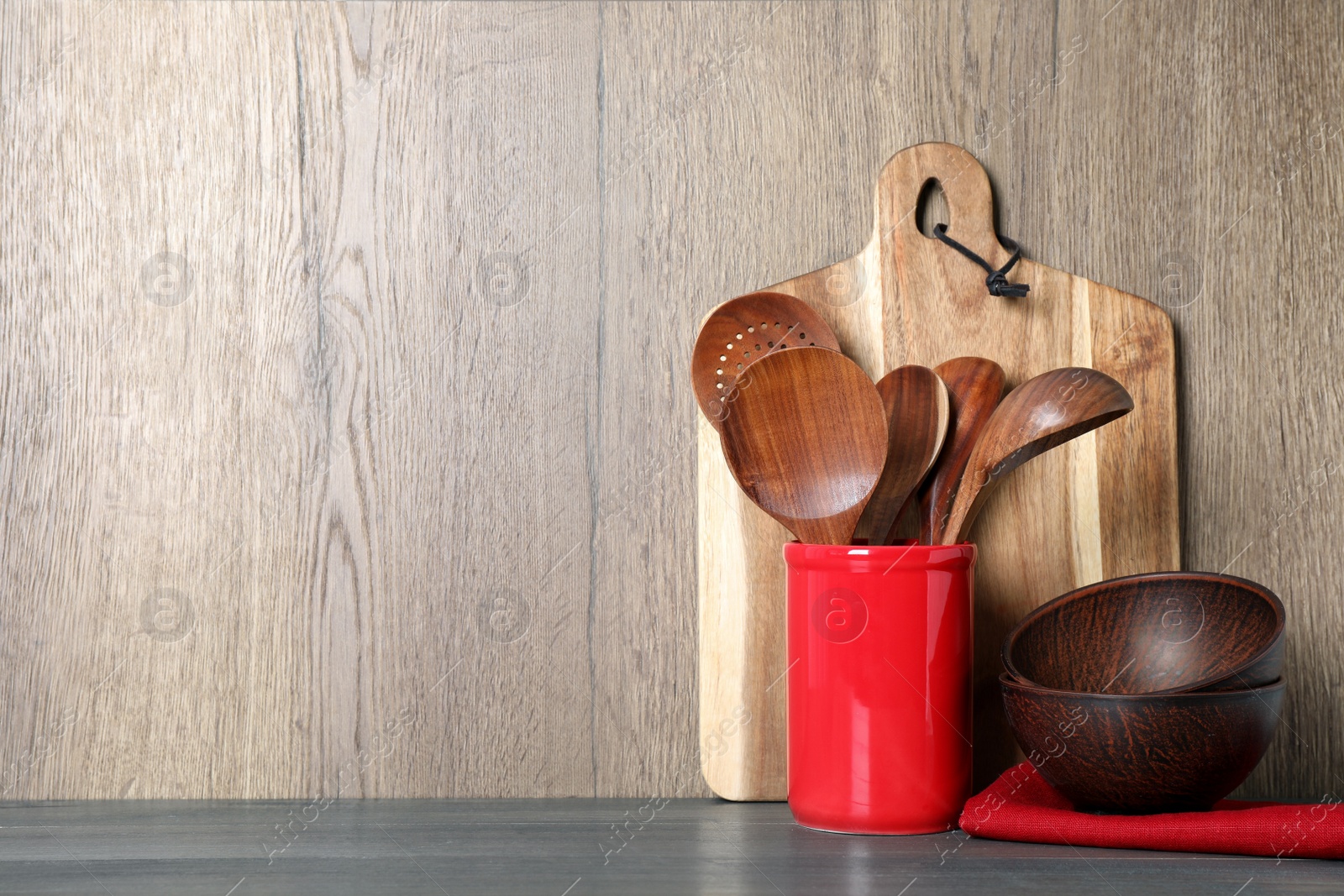 Photo of Set of wooden kitchen utensils, board and bowls on grey table. Space for text