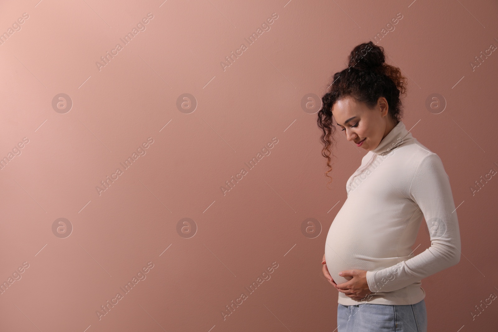 Photo of Pregnant young African-American woman on dusty rose background. Space for text