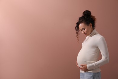 Pregnant young African-American woman on dusty rose background. Space for text