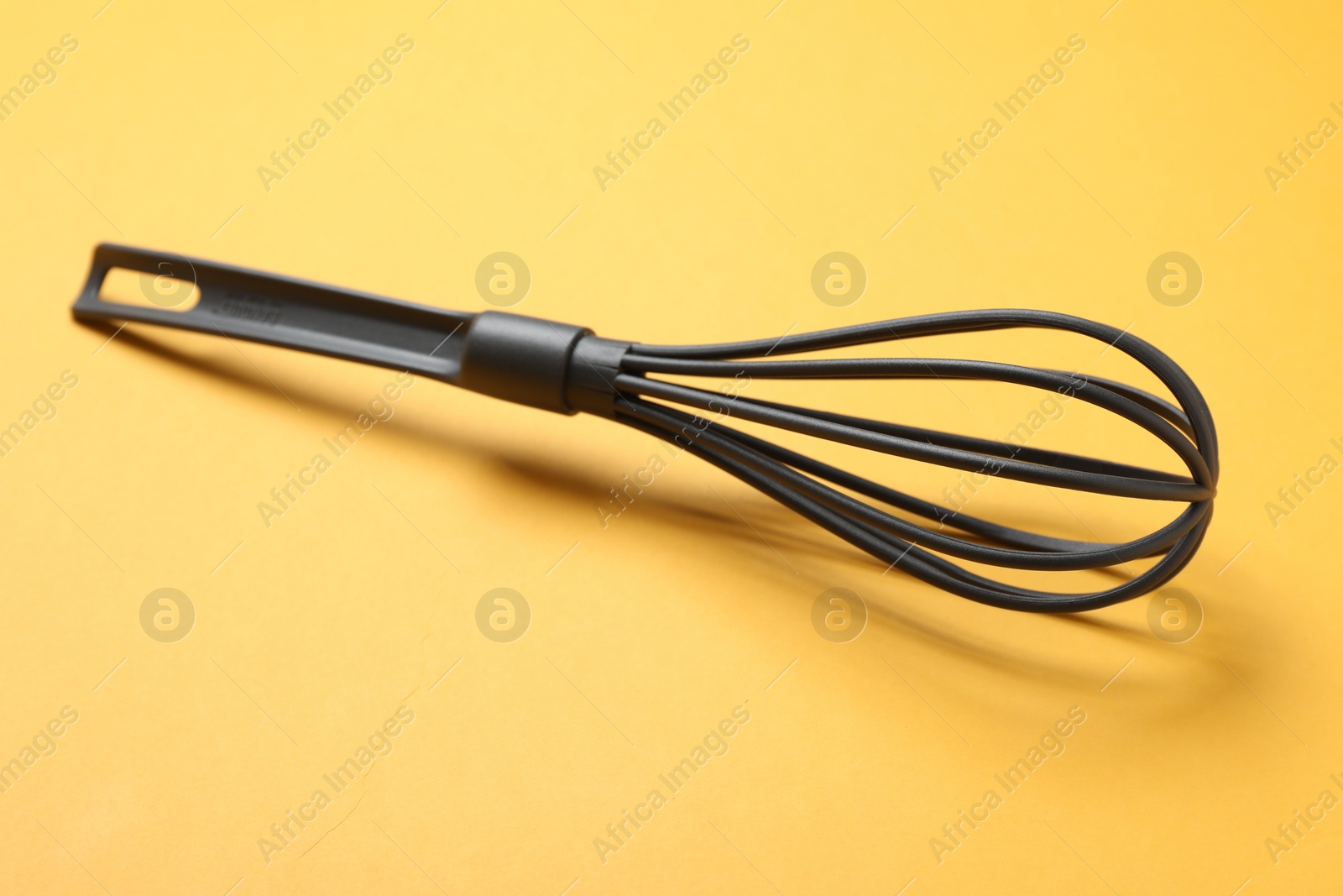 Photo of Plastic whisk on yellow background. Kitchen tool