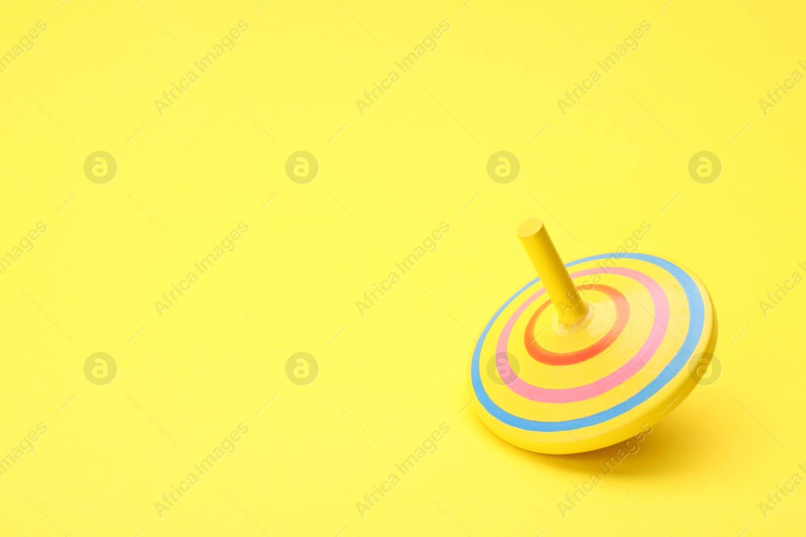 Photo of One bright spinning top on yellow background, space for text. Toy whirligig