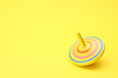 Photo of One bright spinning top on yellow background, space for text. Toy whirligig