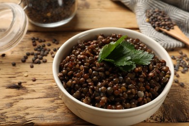 Photo of Delicious lentils with parsley in bowl on wooden table, closeup. Space for text