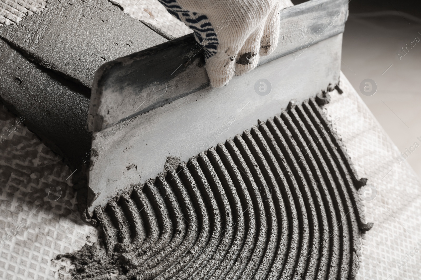 Photo of Worker spreading concrete on ceramic tile with spatula, closeup