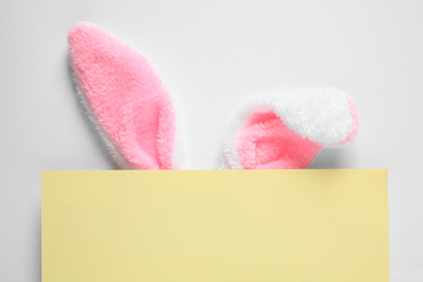 Photo of Decorative bunny ears and yellow card on white background, top view. Easter holiday