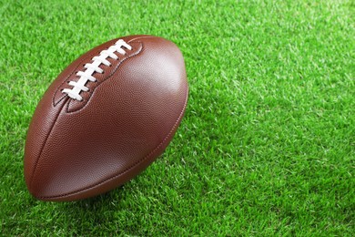 American football ball on green grass, space for text