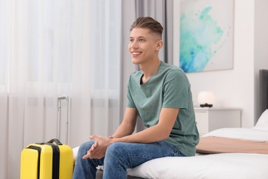 Photo of Smiling guest with suitcase relaxing on bed in stylish hotel room