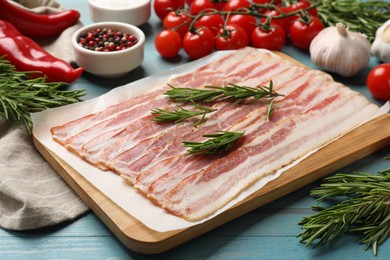 Slices of raw bacon and fresh products on light blue table, closeup