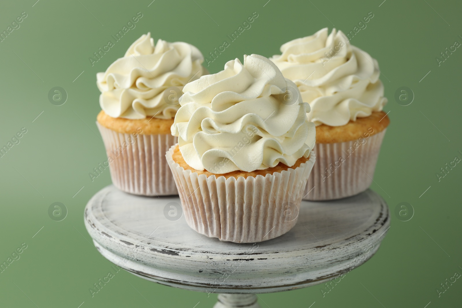 Photo of Tasty vanilla cupcakes with cream on green background, closeup