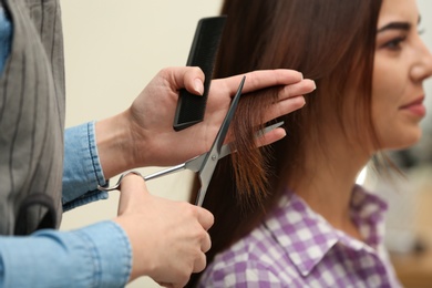 Barber making stylish haircut with professional scissors in beauty salon, closeup