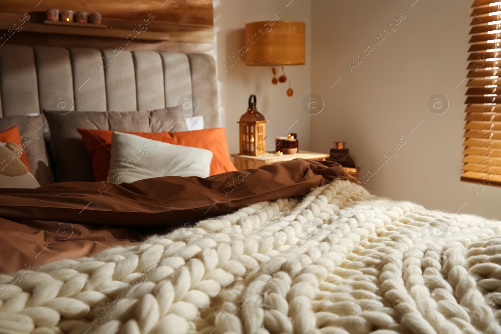 Photo of Bed with knitted blanket and cushions in room. Interior design
