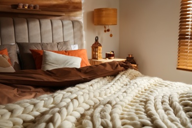 Photo of Bed with knitted blanket and cushions in room. Interior design