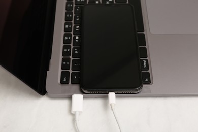 Photo of Smartphone connected with charge cable to laptop on light table, closeup. Space for text