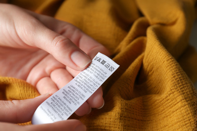Photo of Woman reading clothing label with care instructions on yellow garment, closeup