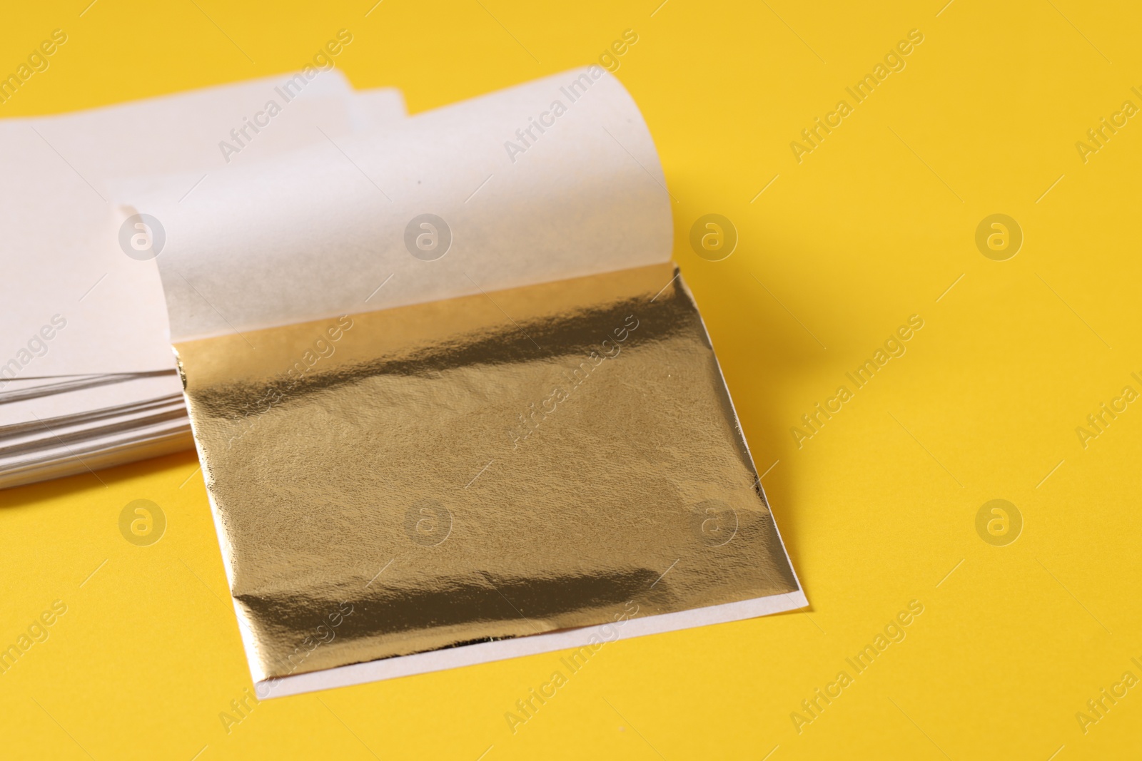 Photo of Edible gold leaf sheets on yellow background, closeup