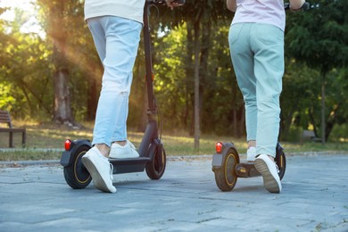 Couple riding modern electric kick scooters in park, back view