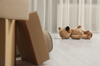 Photo of Cute lonely teddy bear on floor near boxes indoors
