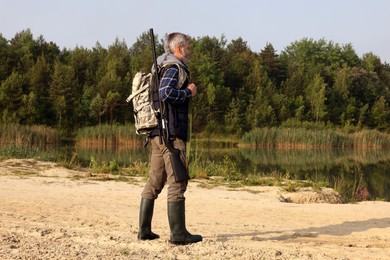 Photo of Man with hunting rifle near lake outdoors. Space for text