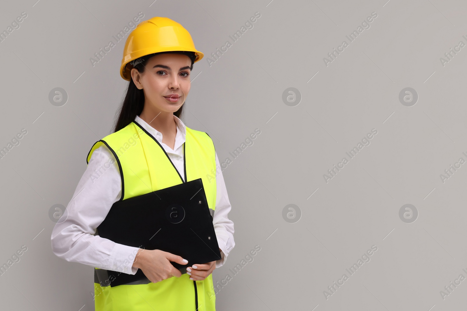 Photo of Engineer in hard hat holding clipboard on grey background, space for text