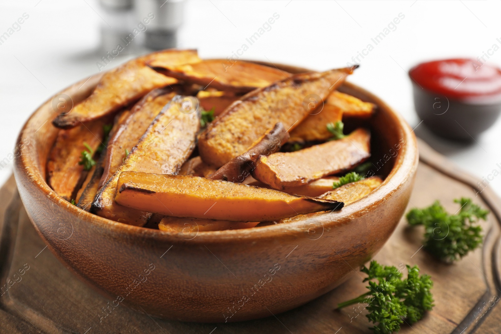 Photo of Bowl with tasty sweet potato fries on wooden board, closeup