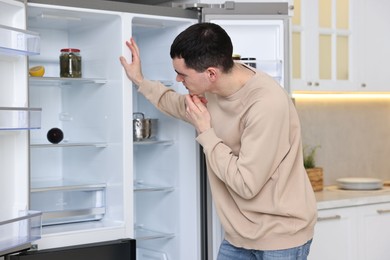 Photo of Thoughtful man near empty refrigerator in kitchen at home