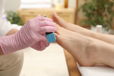 Photo of Professional pedicurist filing client`s toenails in beauty salon, closeup