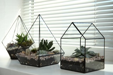 Photo of Glass florarium vases with succulents on white windowsill indoors