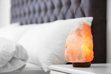 Himalayan salt lamp on table in bedroom. Space for text