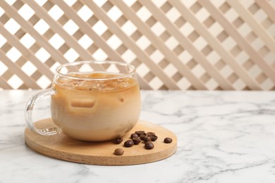 Photo of Refreshing iced coffee with milk in glass cup and beans on white marble table, space for text