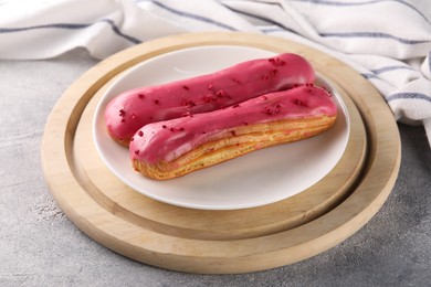 Plate with tasty glazed eclairs on grey textured table, closeup