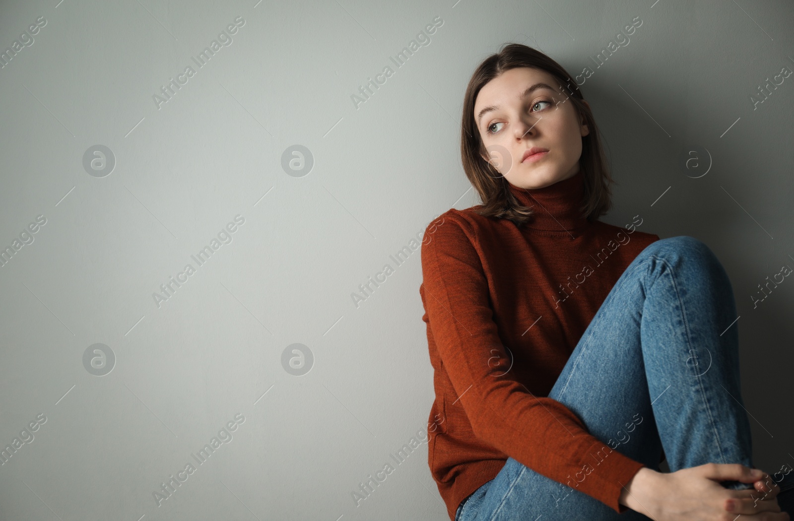 Photo of Sad young woman near grey wall, space for text