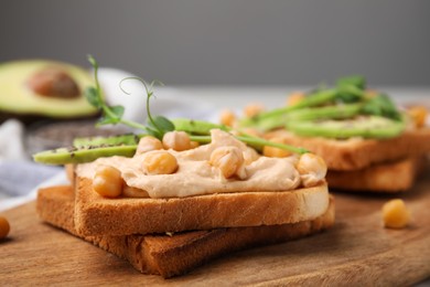 Photo of Delicious sandwiches with hummus, avocado and chickpeas on wooden board, closeup