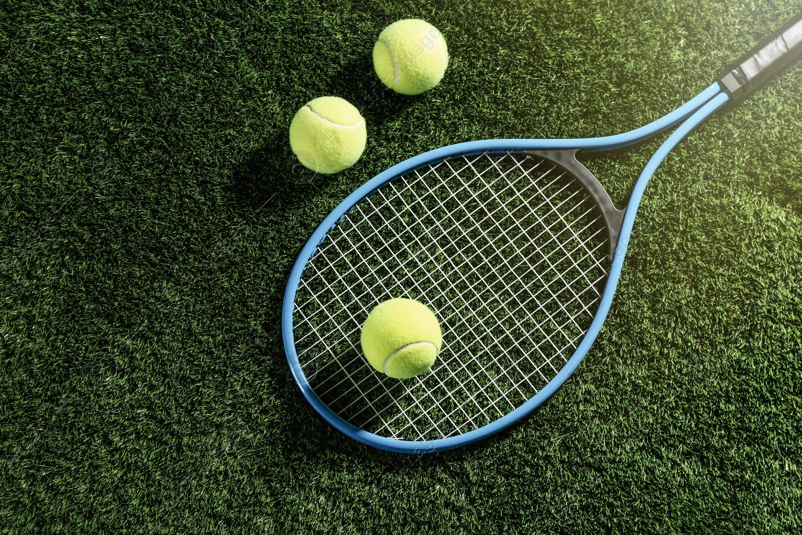 Photo of Tennis racket and balls on green grass, flat lay. Sports equipment