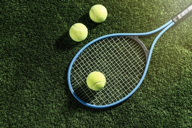 Photo of Tennis racket and balls on green grass, flat lay. Sports equipment