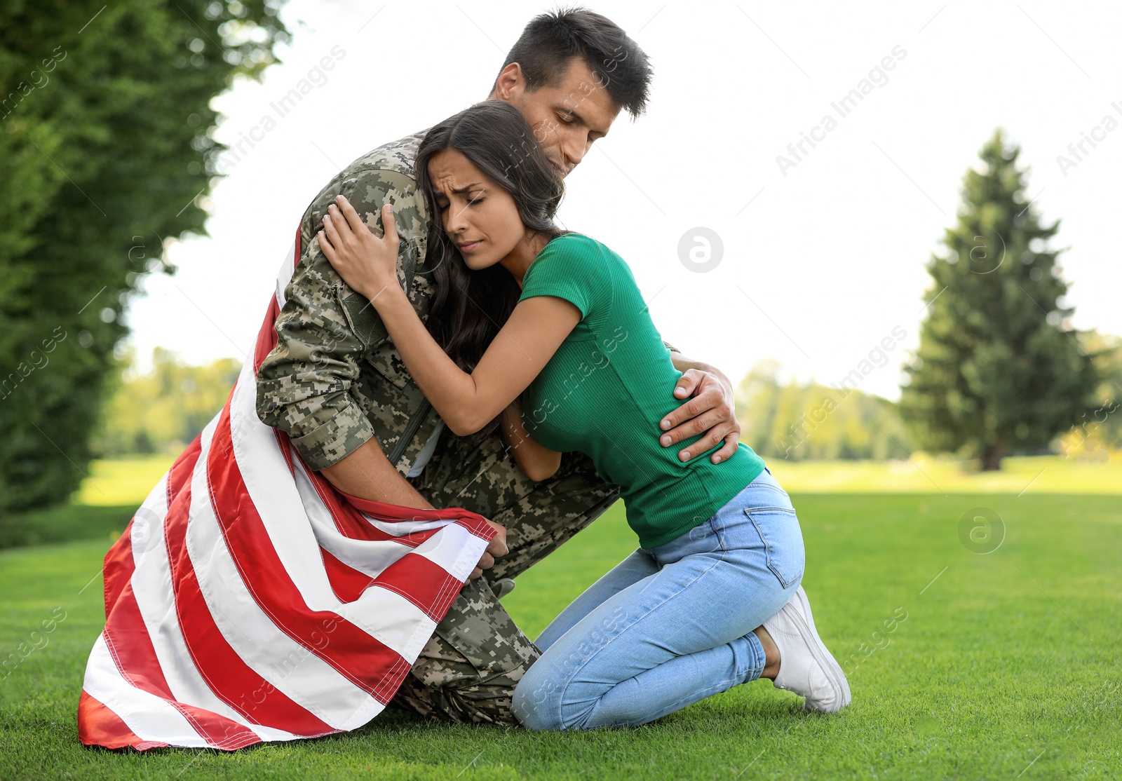 Photo of Man in military uniform with American flag hugging his wife at green park