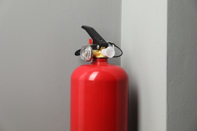 Photo of One fire extinguisher near grey wall indoors