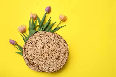 Photo of Tasty matzos and fresh flowers on yellow background, flat lay with space for text. Passover (Pesach) celebration
