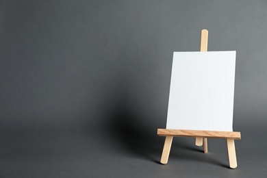 Wooden easel with blank canvas board on dark background, space for text. Children's painting