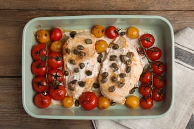 Delicious chicken fillets with capers, tomatoes and sauce in baking dish on wooden table, top view