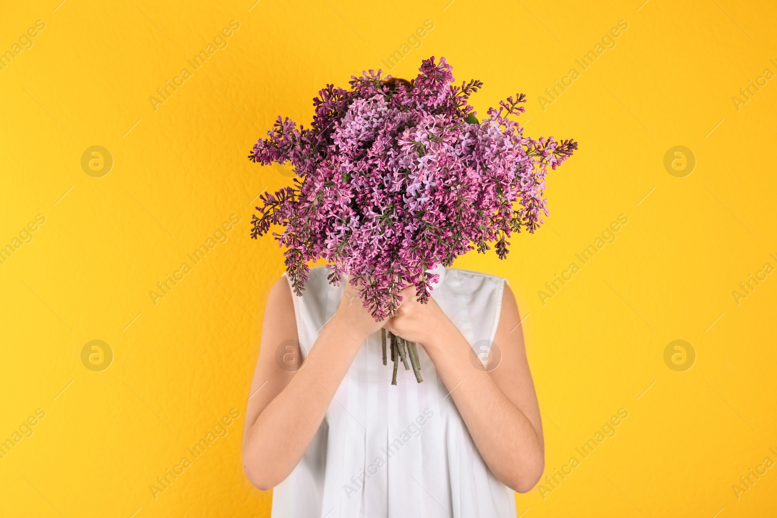 Photo of Woman closing face with bouquet of beautiful lilac flowers on color background