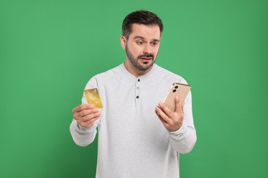 Photo of Confused man with credit card and smartphone on green background. Debt problem