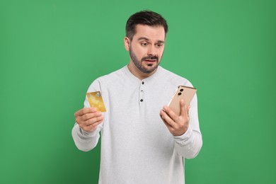 Confused man with credit card and smartphone on green background. Debt problem