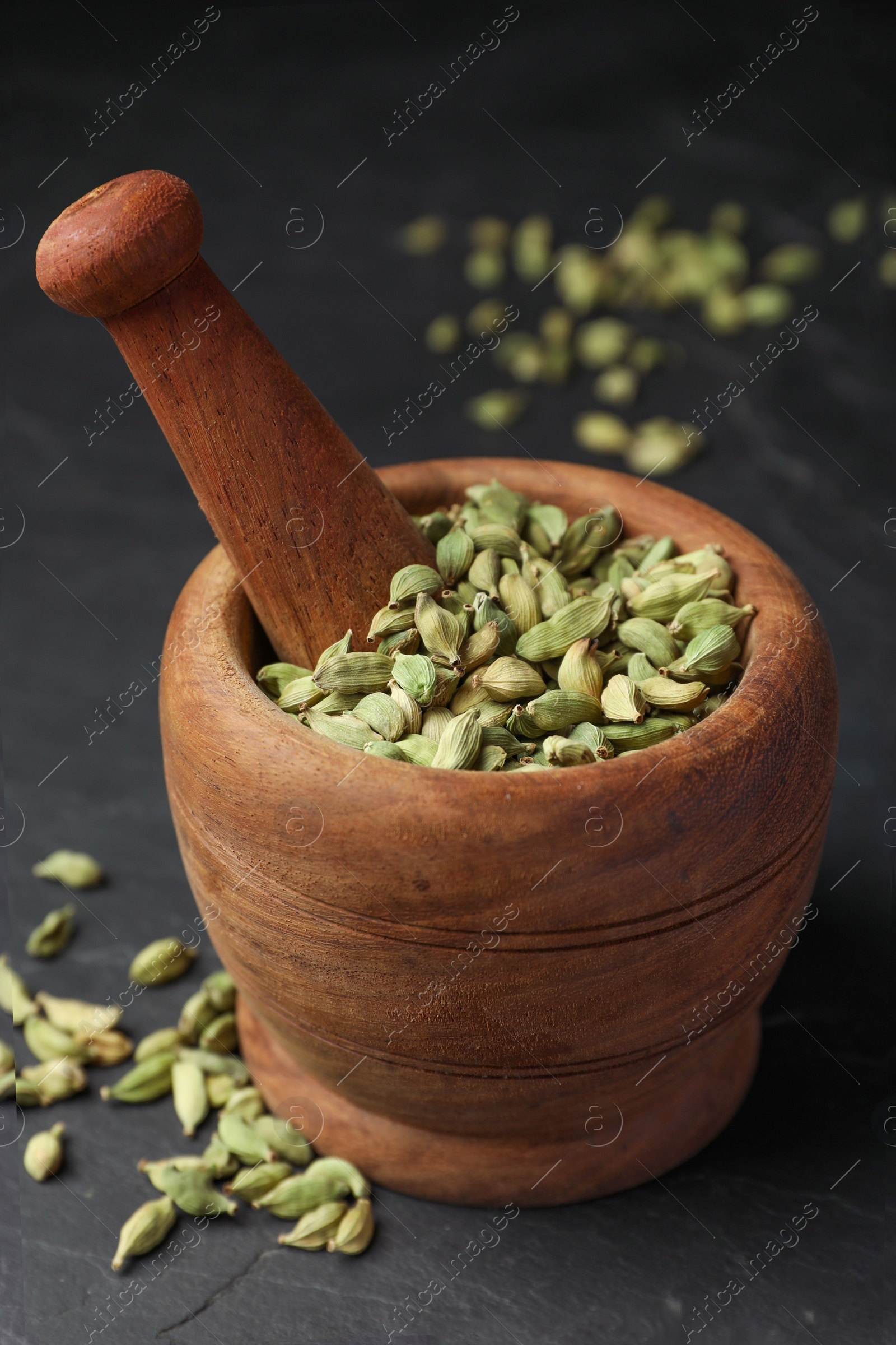 Photo of Mortar with pestle and dry cardamom pods on dark grey table, closeup