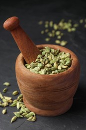 Photo of Mortar with pestle and dry cardamom pods on dark grey table, closeup