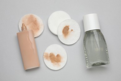 Bottle of makeup remover, foundation, clean and dirty cotton pads on light grey background, flat lay